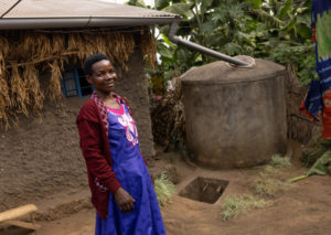 A Rwandan woman in front of a household rainwater tank.