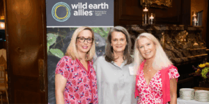 Ginny Busch, Katie Frohardt, and Clea Newman Soderlund in front of a Wild Earth Allies banner